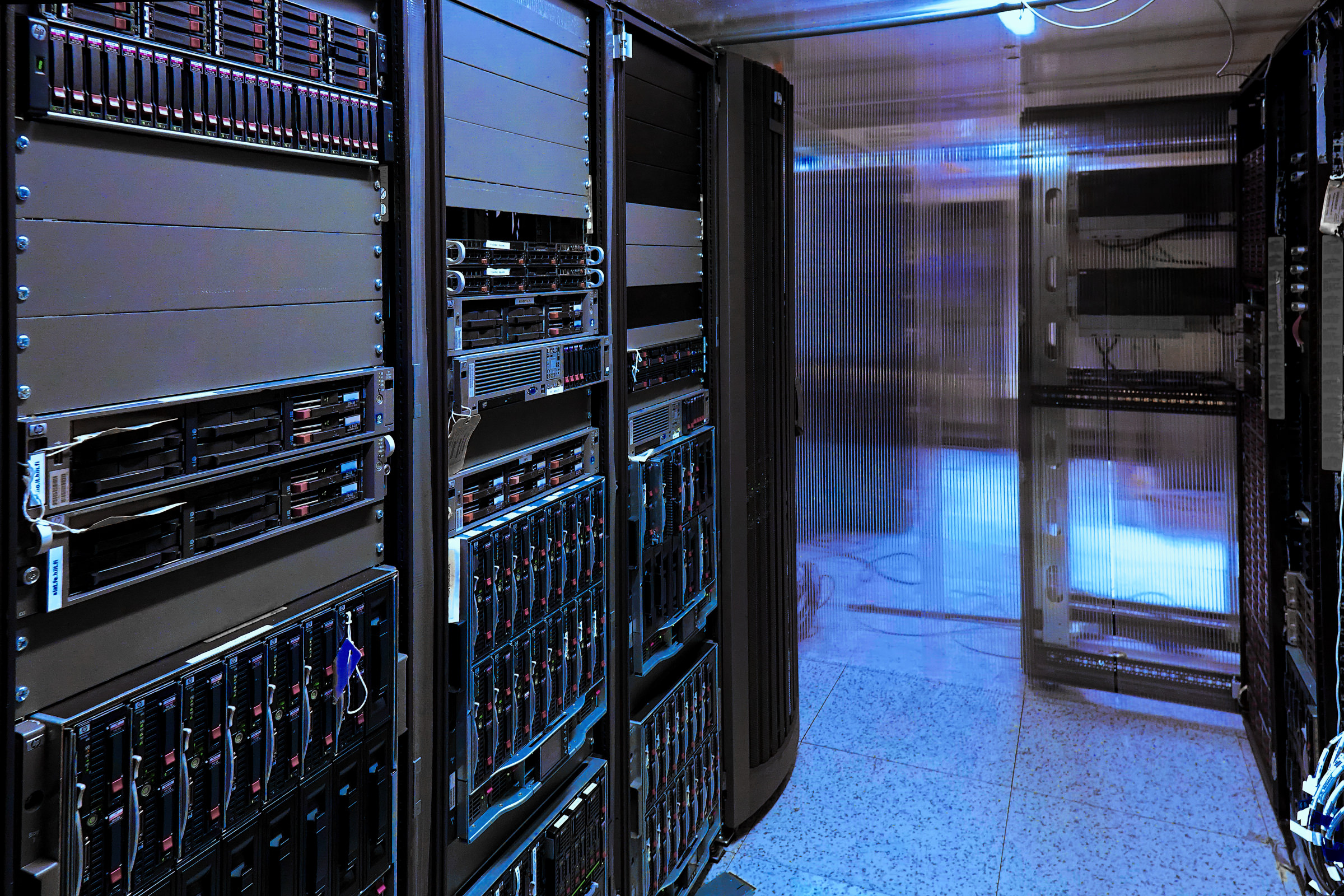 A server room, characterized by rows of computer server racks.
          On the left side, a tall server rack is prominently displayed. 
          It is filled with multiple tiers of server units.
          To the right of the first rack, another server rack is partially visible, also filled with server units and drives. 
	  The arrangement suggests a highly organized and dense installation of computing hardware.