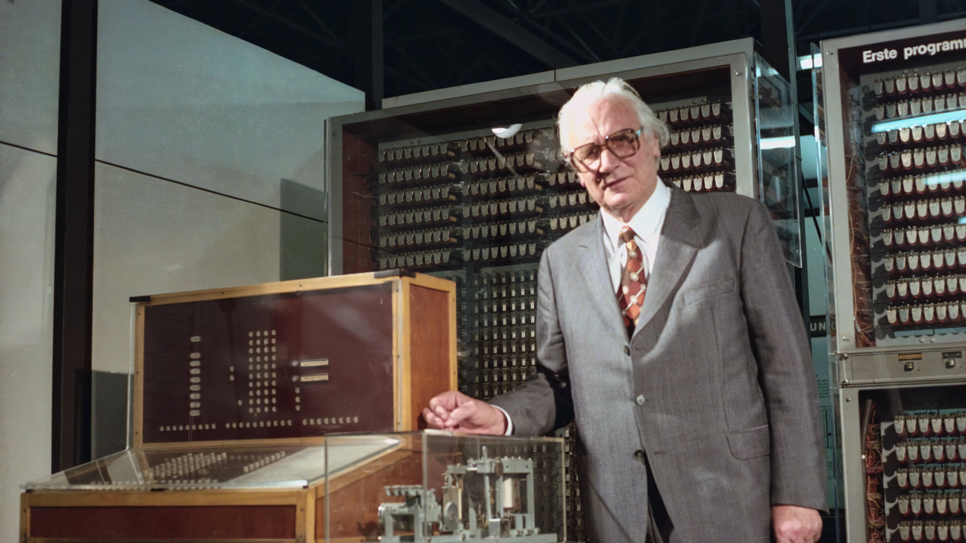 A man standing by a control panel and in front of two cabinets electromechanical relays